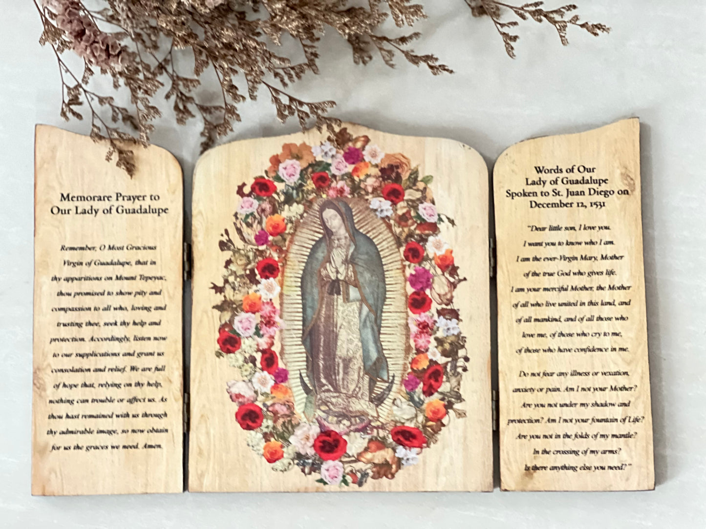 A wooden triptych featuring an image of Our Lady of Guadalupe with floral designs, with inscriptions on the shutters. The left shutter is inscribed with a prayer, while the right shutter has the words of Our Lady to St. Juan Diego.
