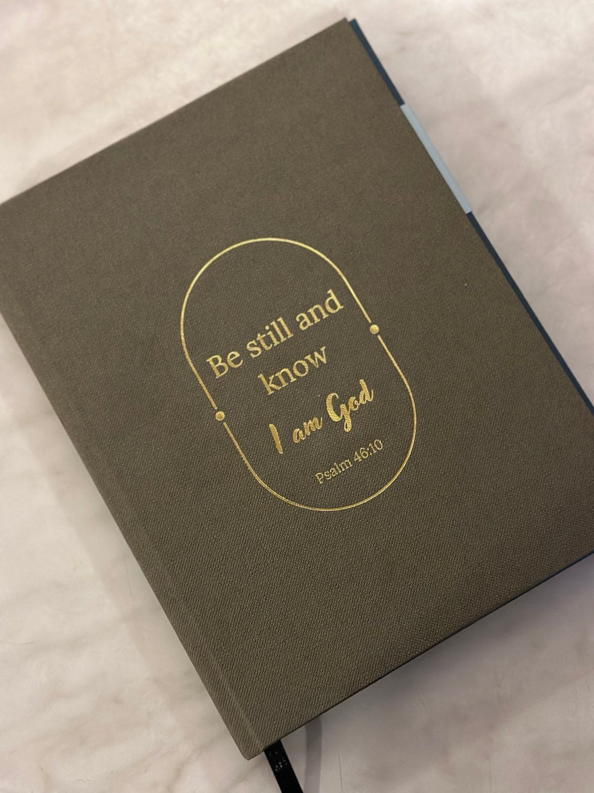 A gray journal with a premium linen material book cover, featuring a quote from Psalm 46:10 'Be still and know I am God' in gold lettering.