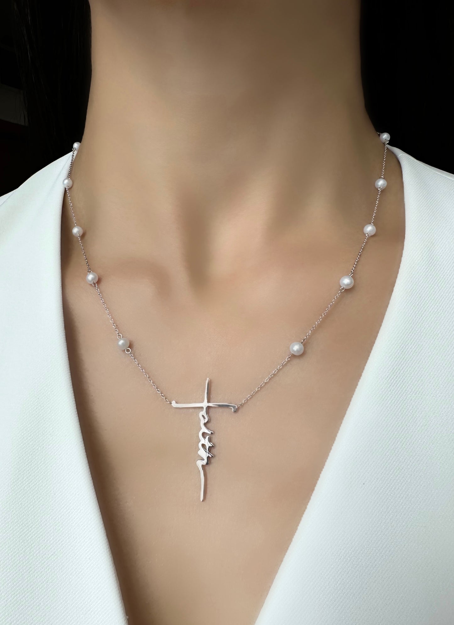 A 14k white gold necklace witch a faith pendant and freshwater pearls, placed on the model.
