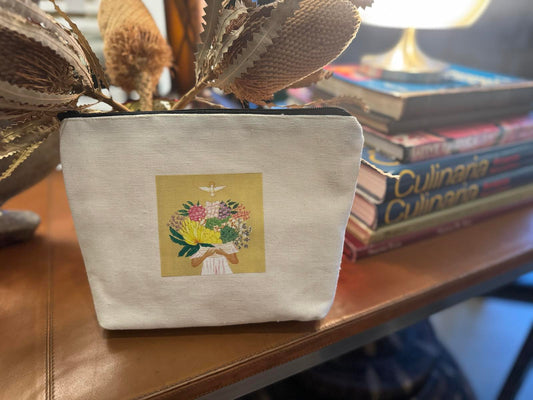 Canvas zippered pouch with a floral design on the front, displayed on a table with a book and a decorative object in the background.