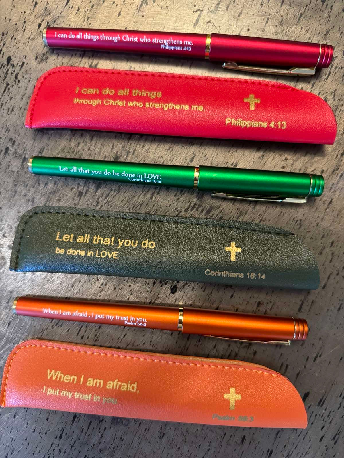 A collection of colored pens with leather sleeves, each inscribed with an inspirational Bible quote.