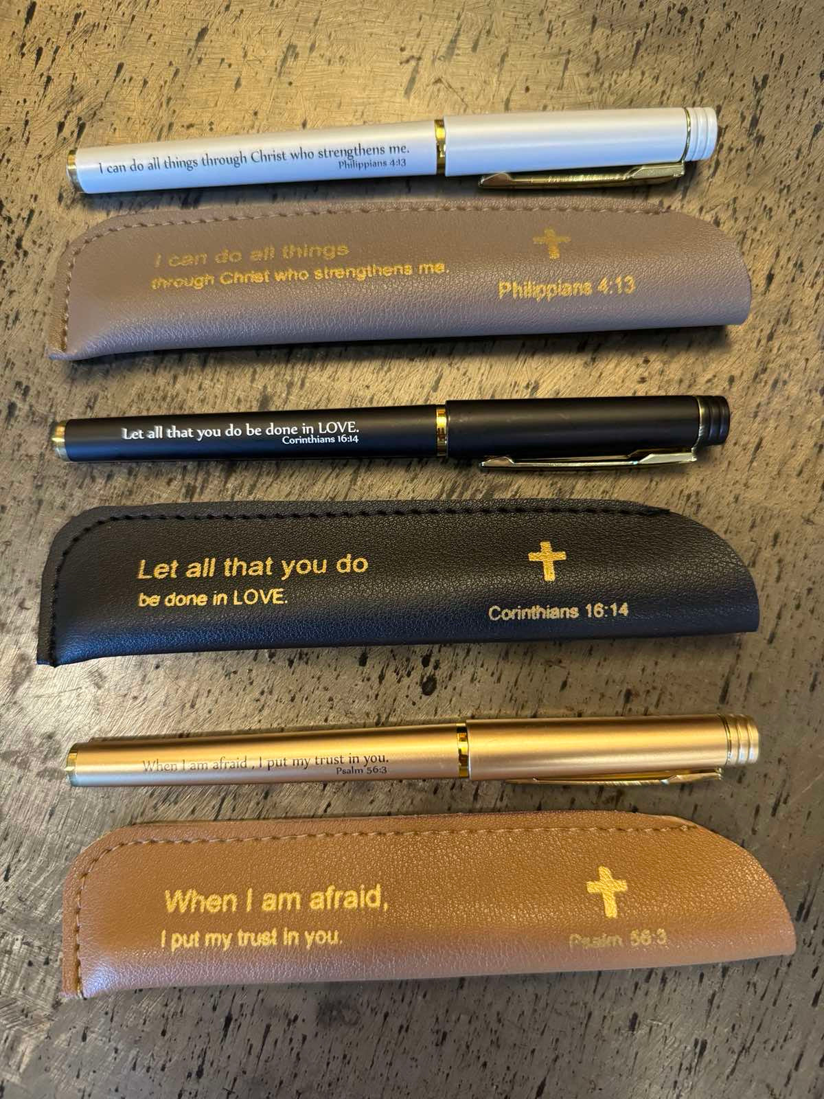 A collection of pens with a neutral color and leather sleeves, each inscribed with an inspirational Bible quote.