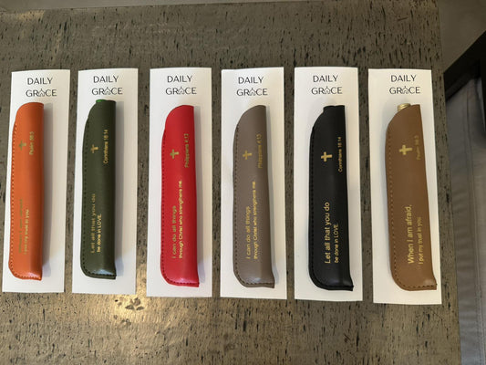 A collection of pens with leather sleeves, each inscribed with an inspirational Bible quote.