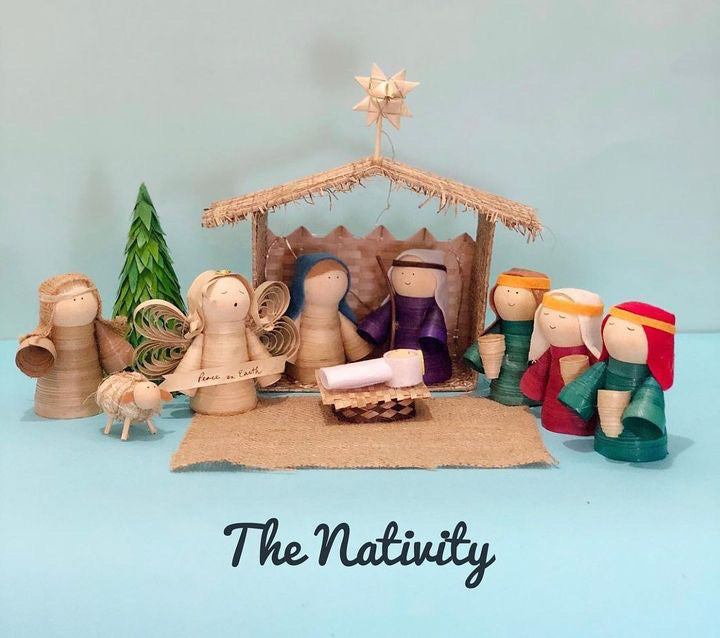 A wooden nativity set featuring various figures including the baby Jesus, Mary, Joseph, and the three Wise Men, with a detached roof and wall, a pine tree, and a burlap mat.