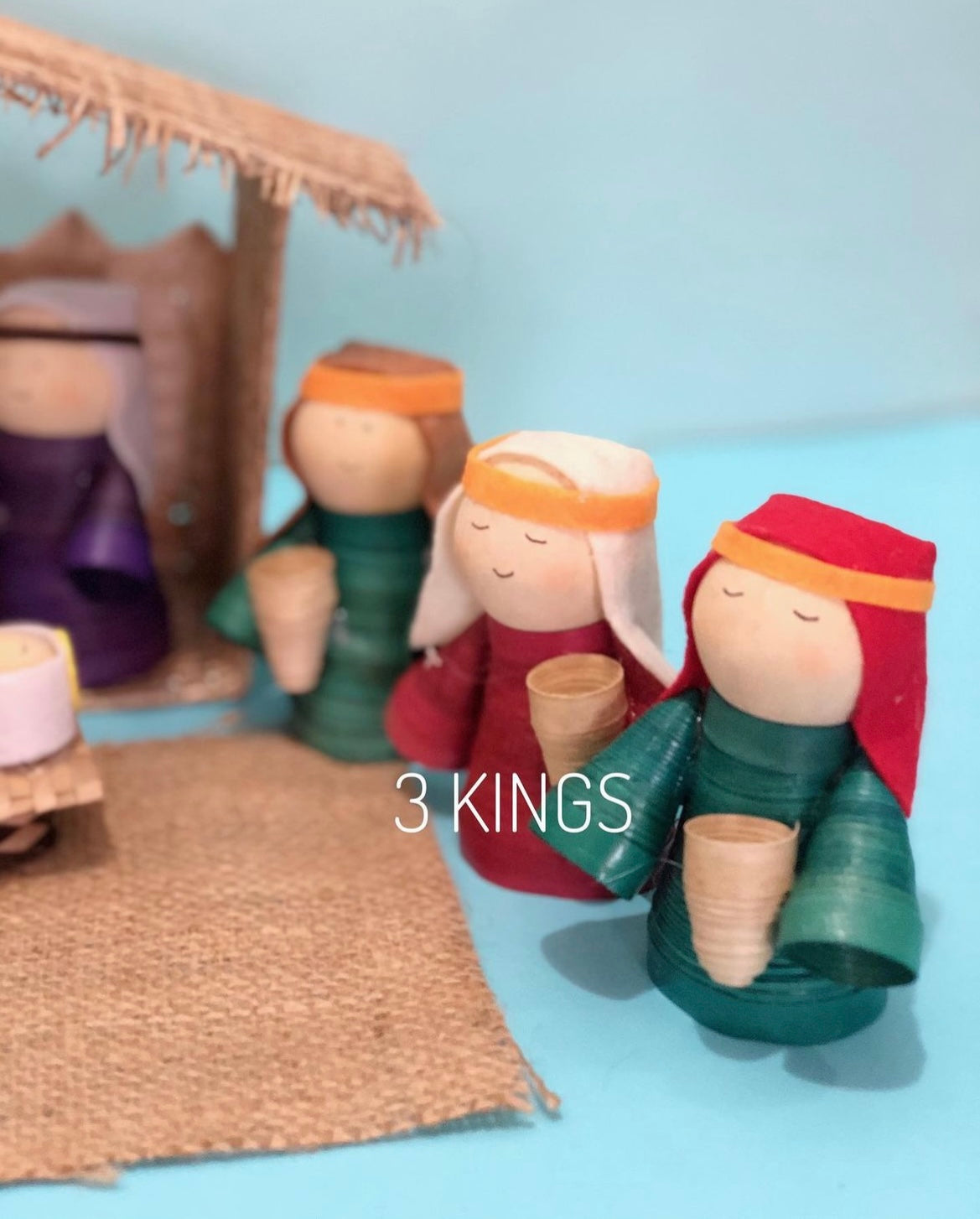 A wooden nativity set featuring the figures three Wise Men, with a detached roof and wall, and a burlap mat.