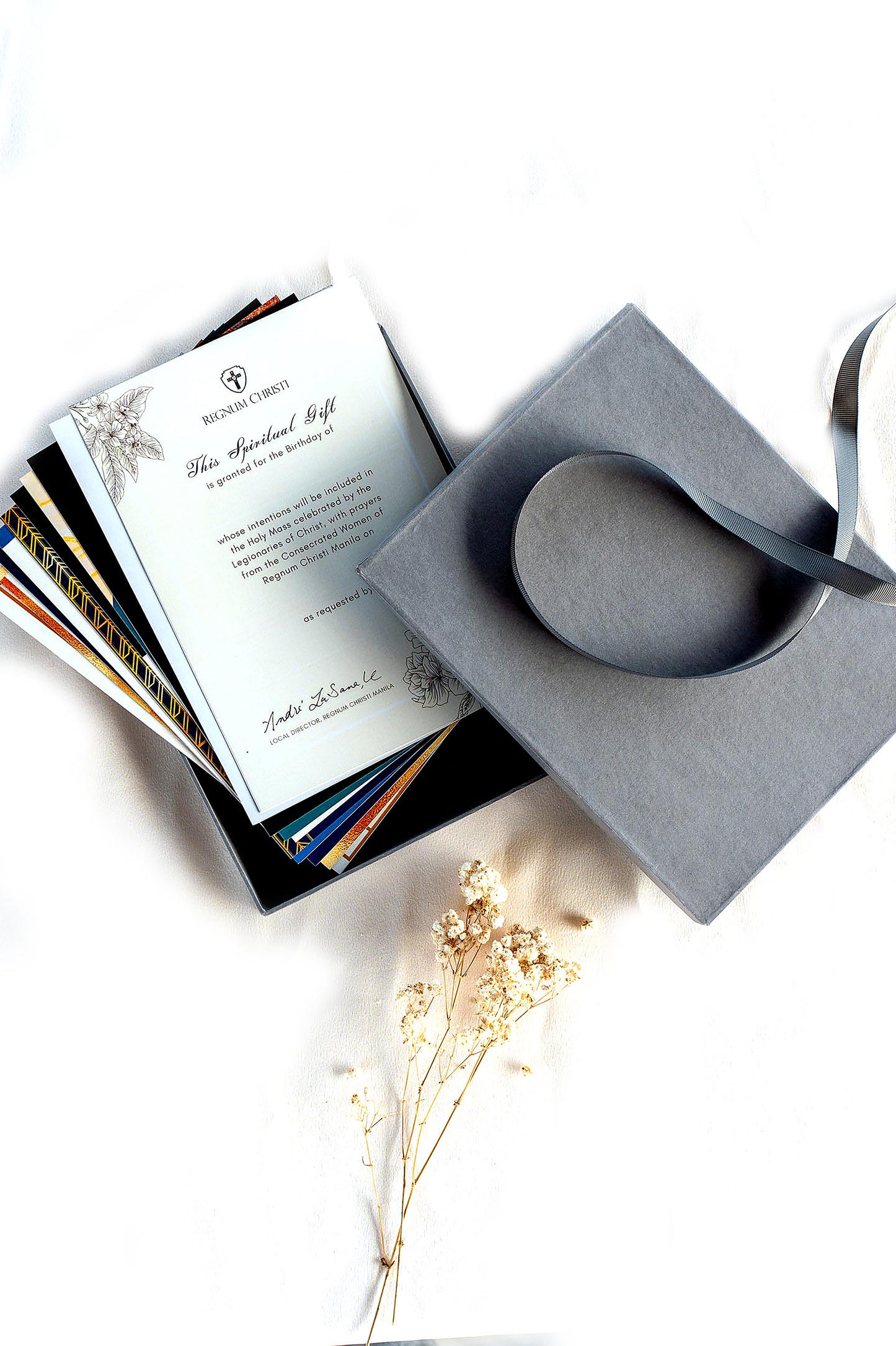 A collection of prayer cards with one card folded on top, placed on a surface and some dried flowers nearby.