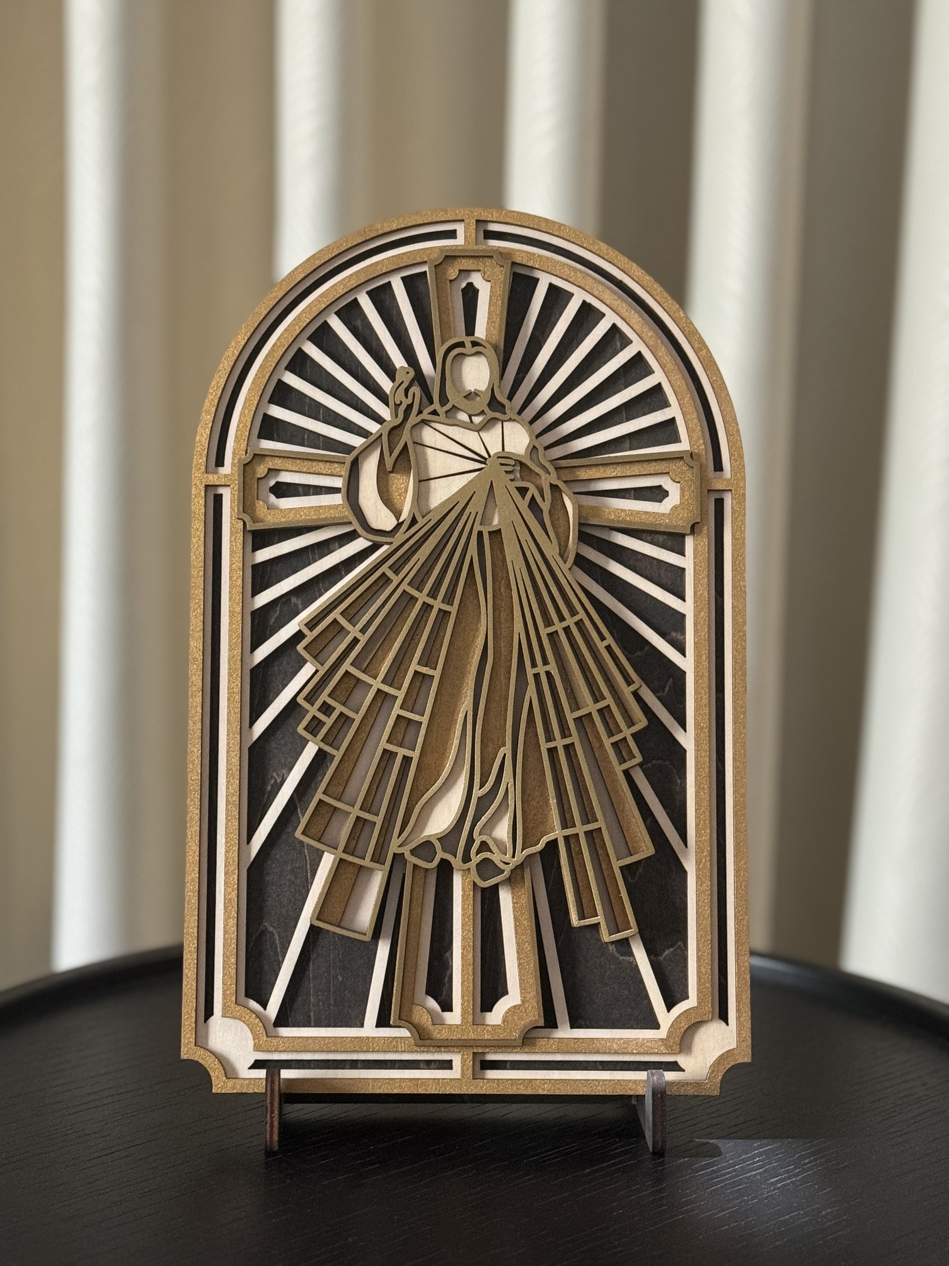 A multi-layered wood art depiction of the Sacred Heart of Jesus Christ, with a gold and white color scheme, placed on a wooden brown table with a neutral background. 