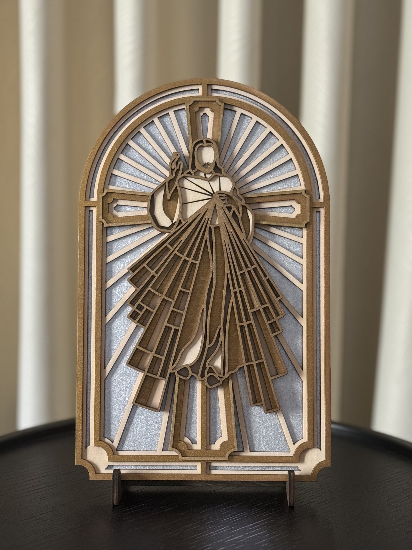 A multi-layered wood art depiction of the Sacred Heart of Jesus Christ, with a gold and white color scheme, placed on a wooden round table with a neutral color.
