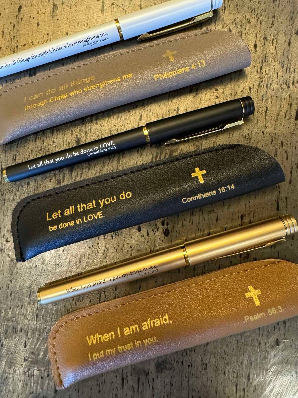 A collection of neutral pens with leather sleeves, each inscribed with an inspirational Bible quote.