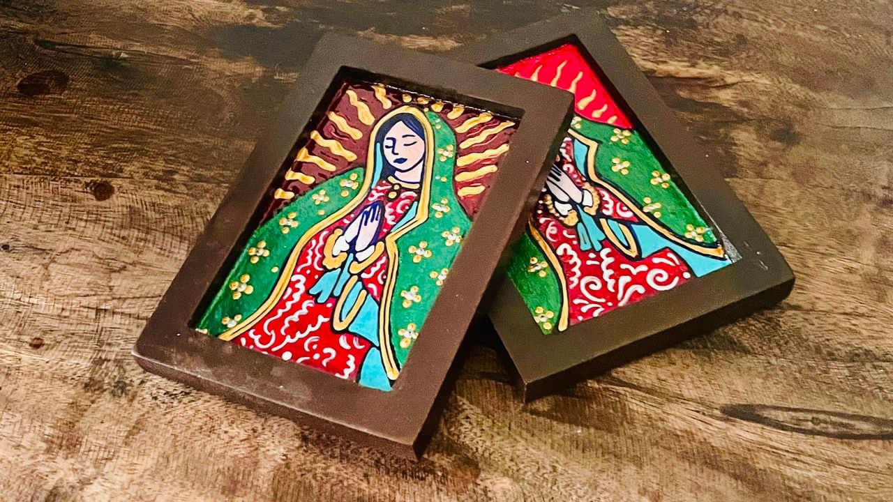 Two hand-painted wooden Estampita with a colorful figure of Our Lady of Guadalupe and traditional design, displayed on a wooden surface.