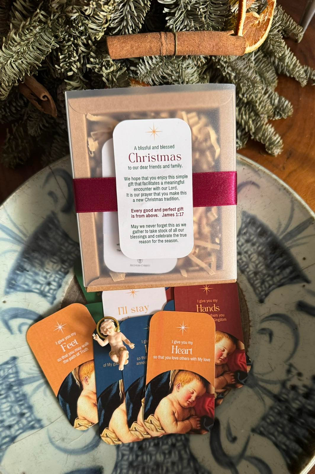 A set of Christmas cards displayed on a table with a statue of Infant Jesus, instruction guide, and decorative items in the background.