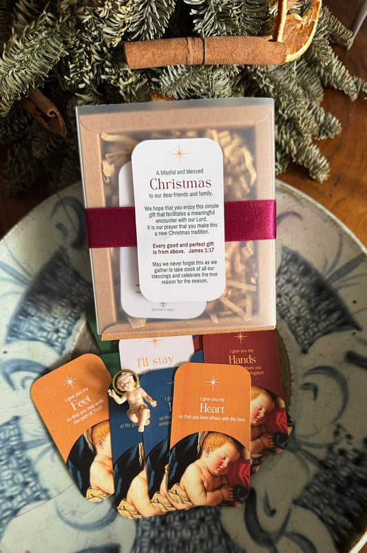 A set of Christmas cards displayed on a table with a statue of Infant Jesus, instruction guide, and decorative items in the background.