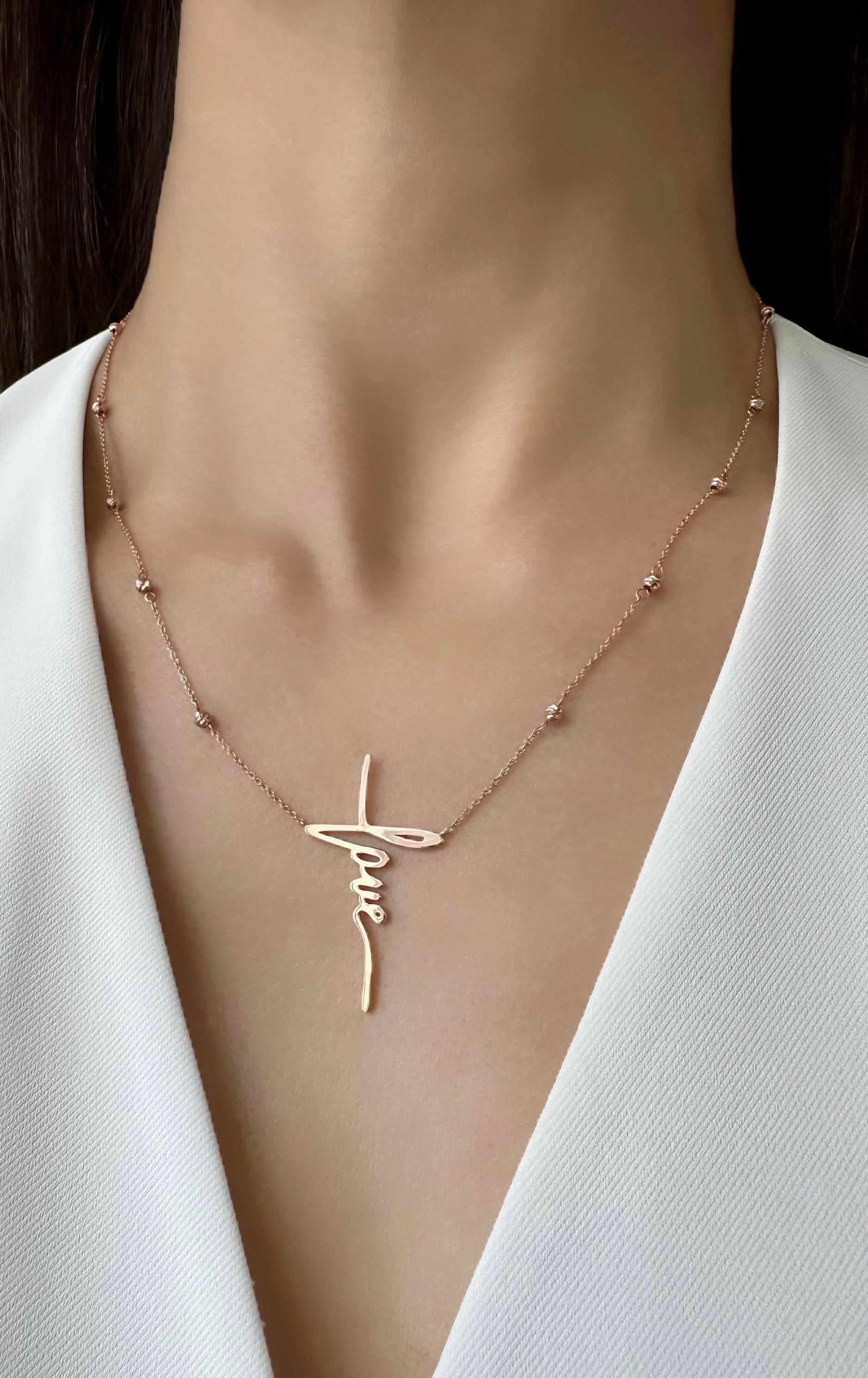 A rose gold necklace with gold beads and a love pendant, displayed on a woman neck.