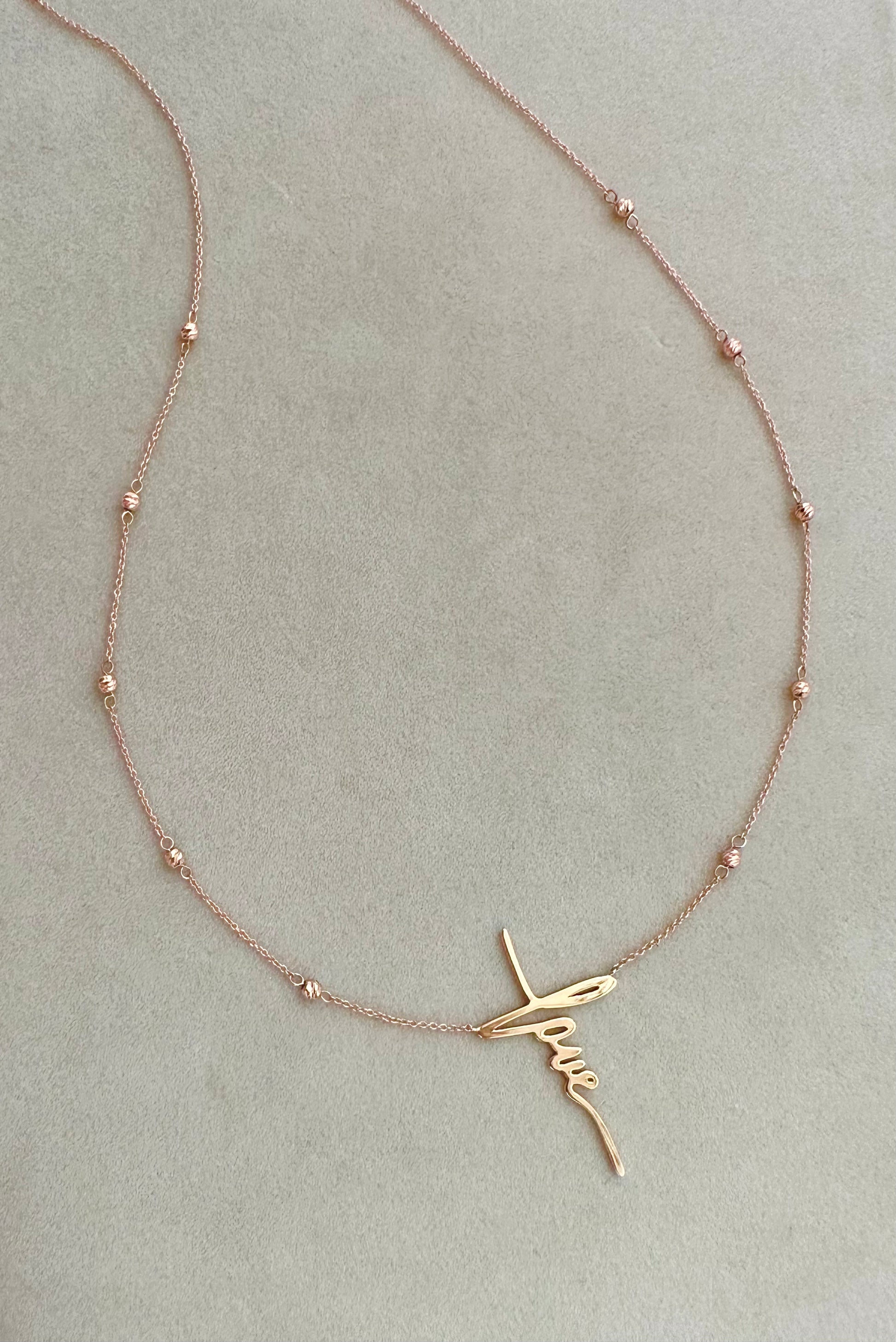 A rose gold necklace with gold beads and a love pendant.