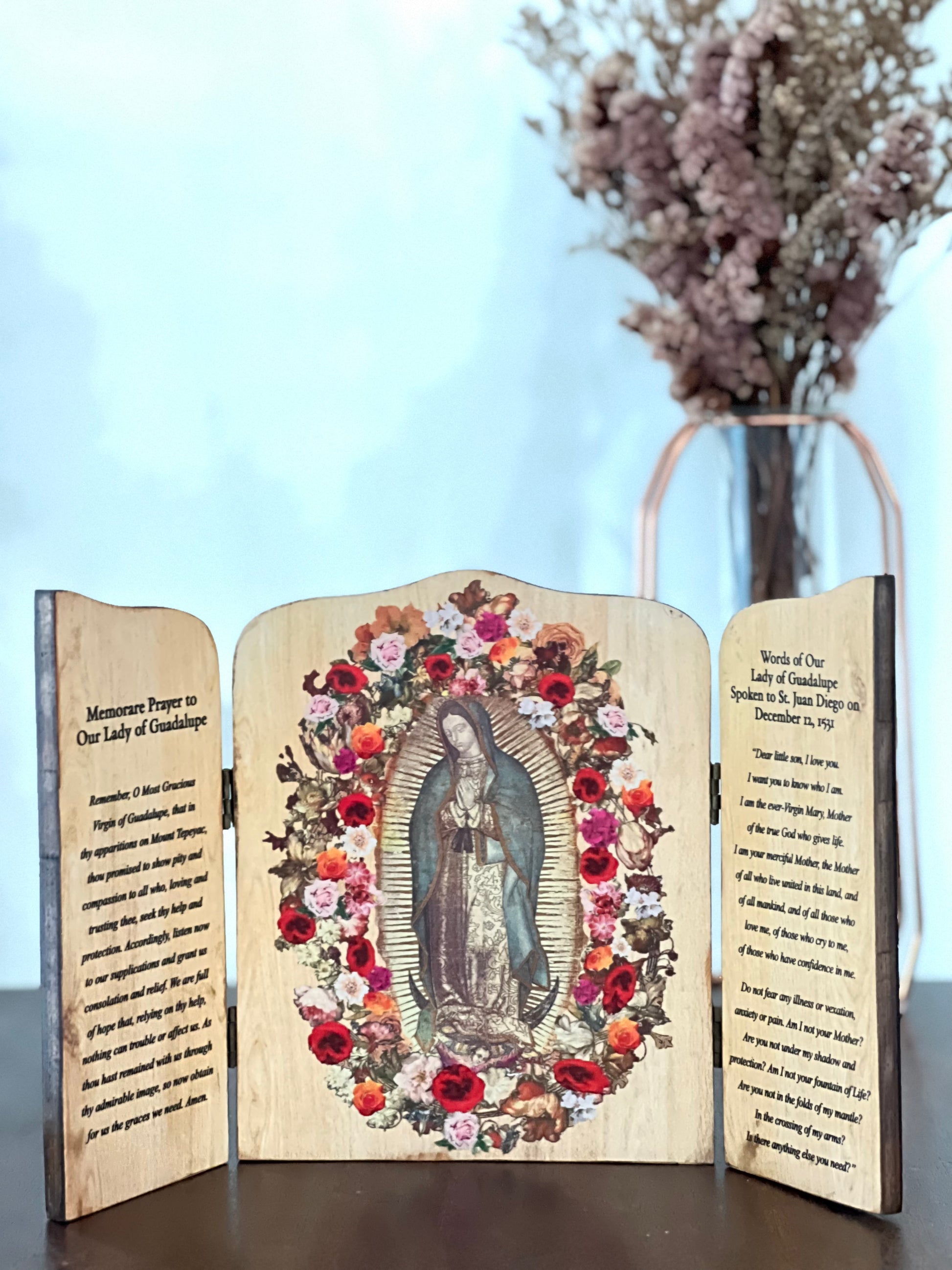 A wooden triptych featuring an image of Our Lady  of Guadalupe with floral designs, with inscriptions on the shutters. The left shutter is inscribed with a prayer, while the right shutter has the words of Our Lady to St. Juan Diego.