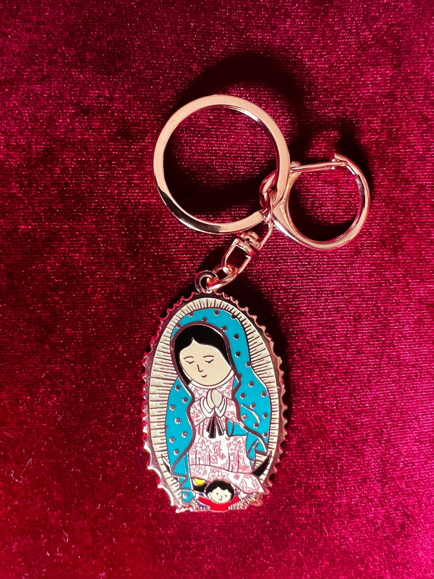 A key chain featuring a bronze-colored Our Lady of Guadalupe together placed on a red surface. 