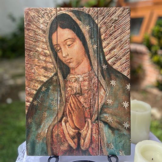 A wooden tablet artwork depicting Our Lady of Guadalupe with a rustic brown frame, placed on a stand.