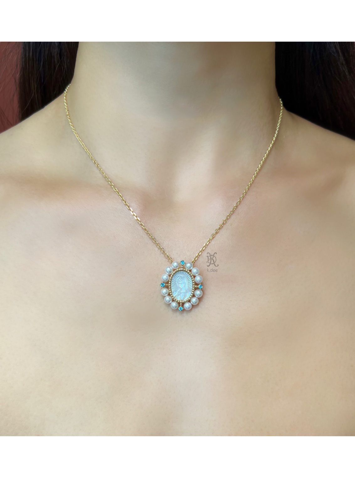 A gold necklace with a pendant featuring a hand-carved mother-of-pearl portrait of Our Lady of Guadalupe, surrounded by blue topaz stones and fresh water pearls. Displayed in the neck of a women.  