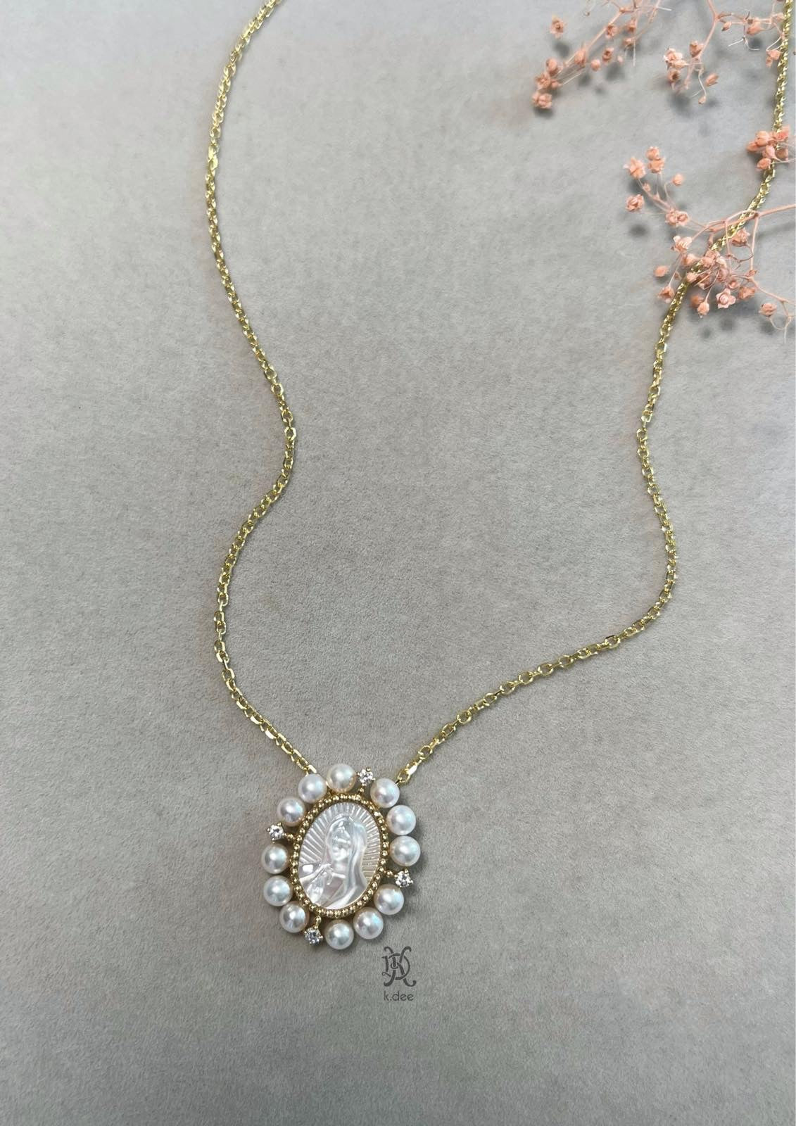 A 1-inch oval pendant of Our Lady of Guadalupe, hand-carved from mother-of-pearl, in 14K yellow gold, displayed on a gold chain.