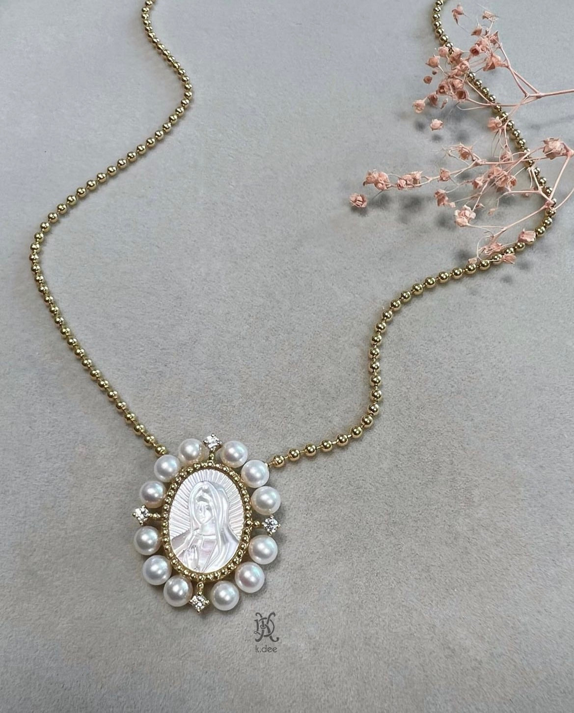 A 1-inch oval pendant of Our Lady of Guadalupe, hand-carved from mother-of-pearl, in 14K yellow gold, displayed on a gold chain.