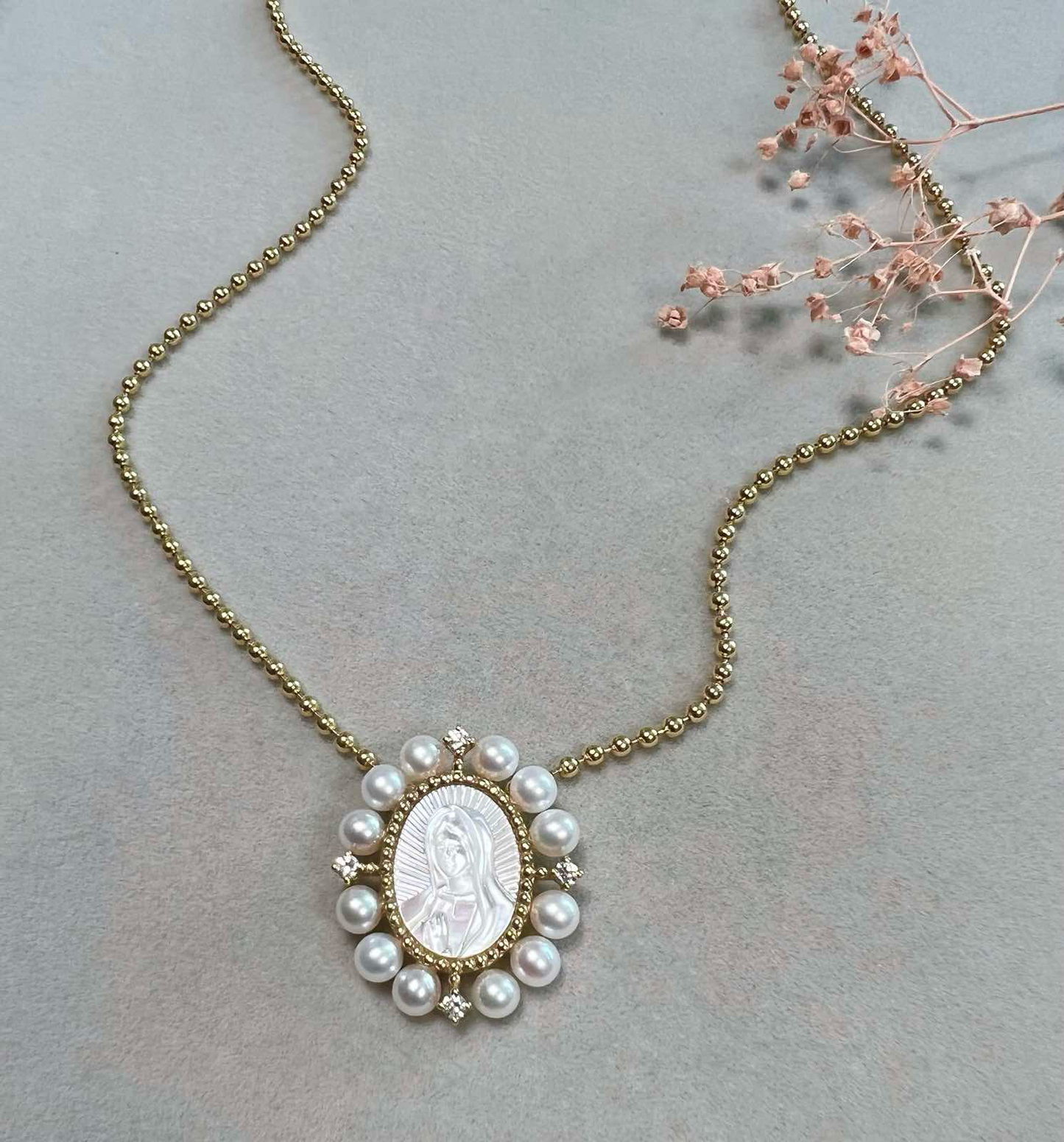 A 1-inch oval pendant of Our Lady of Guadalupe, hand-carved from mother-of-pearl, in 14K yellow gold, displayed on a gold chain.