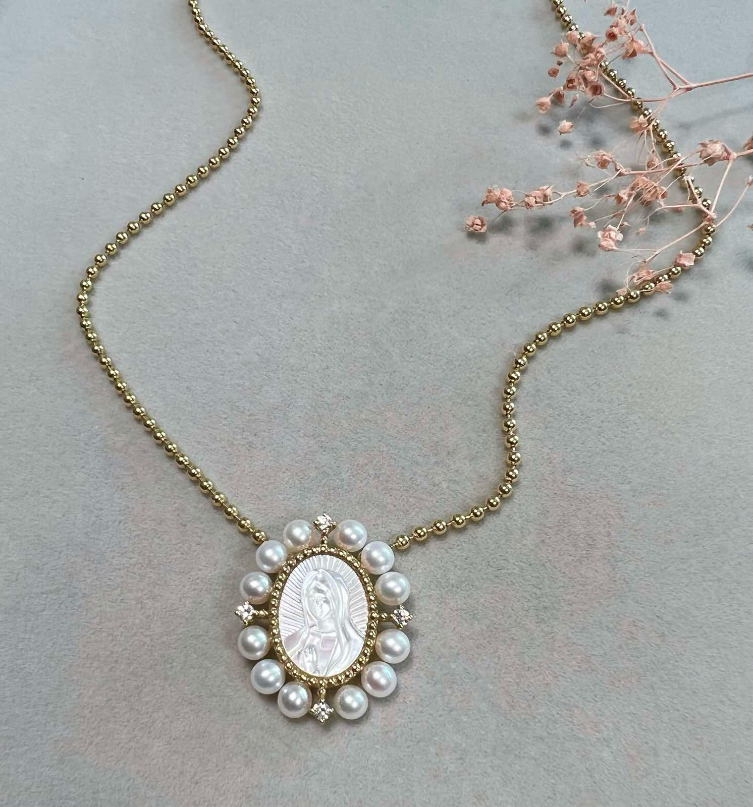 A 1-inch oval pendant of Our Lady of Guadalupe, hand-carved from mother-of-pearl, in 14K yellow gold, displayed on a gold chain.