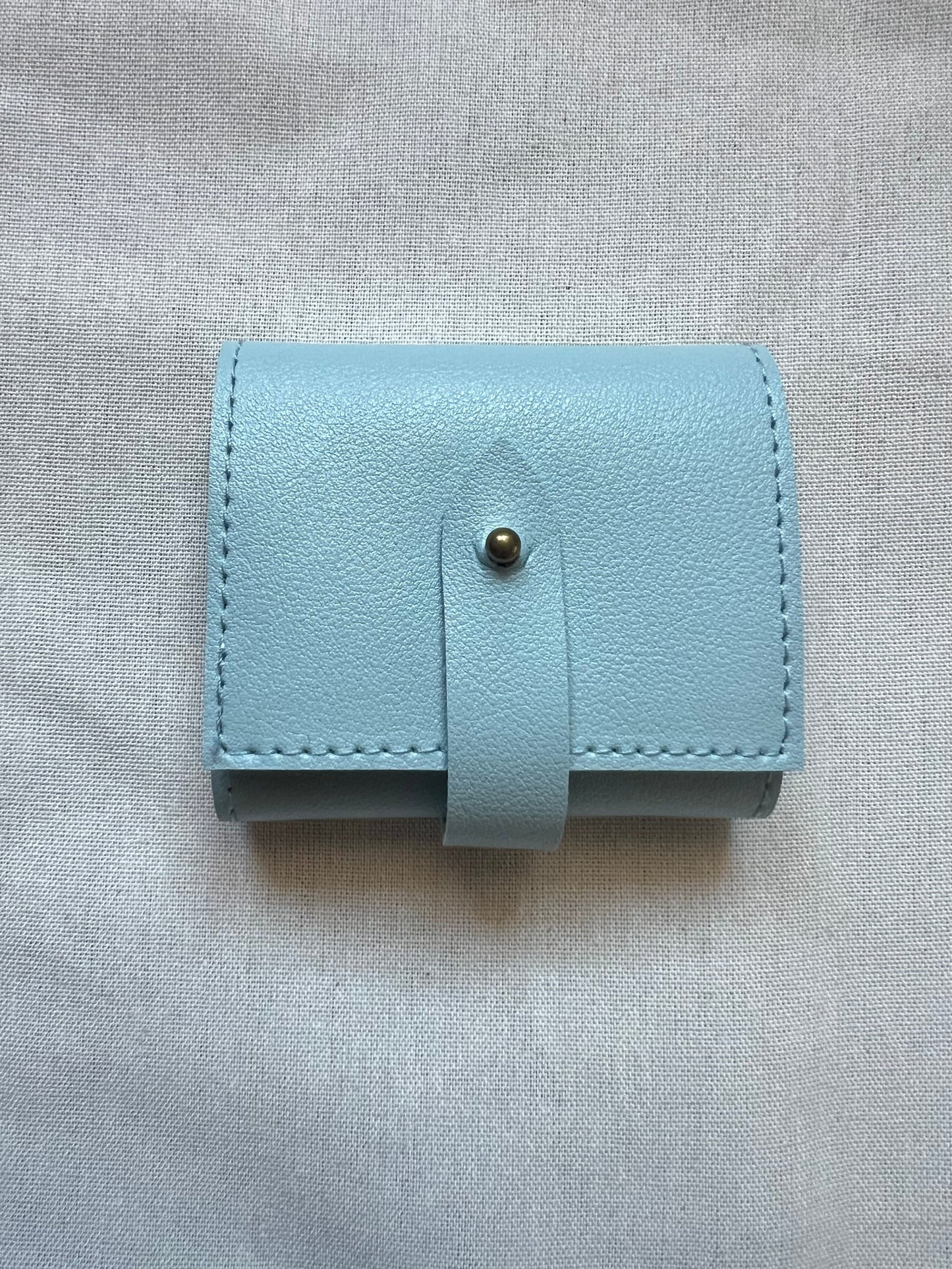 Light blue leather wallet with a button on a gray fabric background