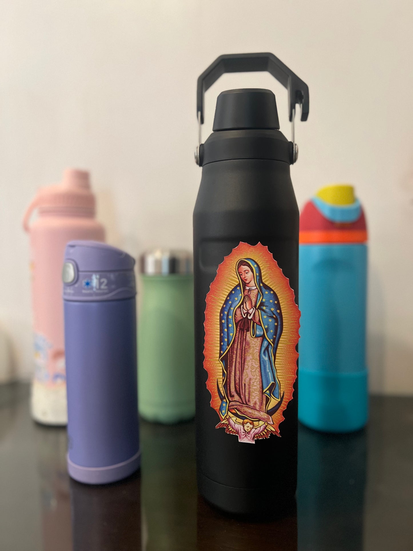 A sticker of Virgin Mary attached on the black tumbler together with the other color of tumbler. 